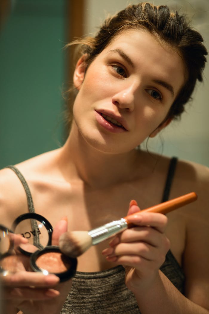 our-services-3 Young woman applying makeup using a brush, focusing on smooth skin and healthy complexion.