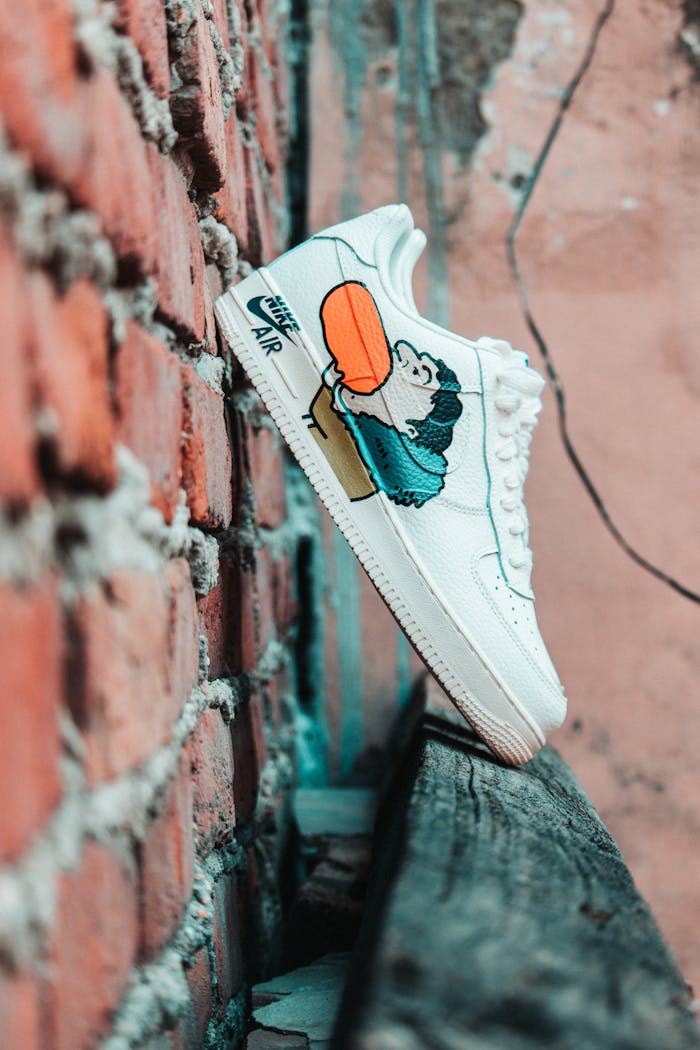 gallery-6 White Nike sneakers with cartoon design against a rough brick wall in urban setting.