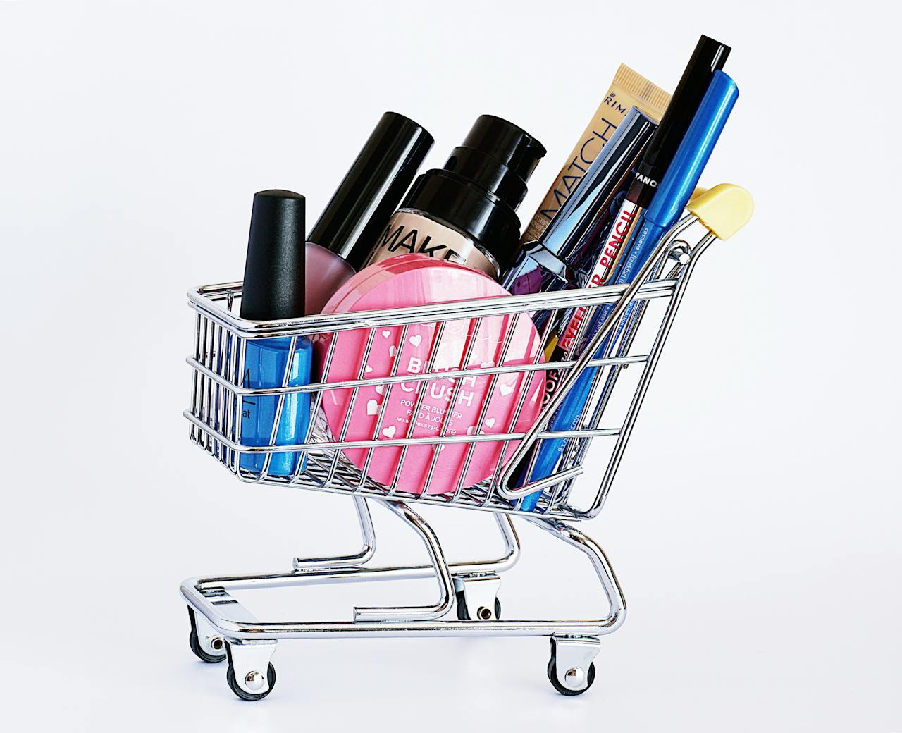 hero-img-01 Miniature shopping cart filled with a variety of cosmetics on a white background.