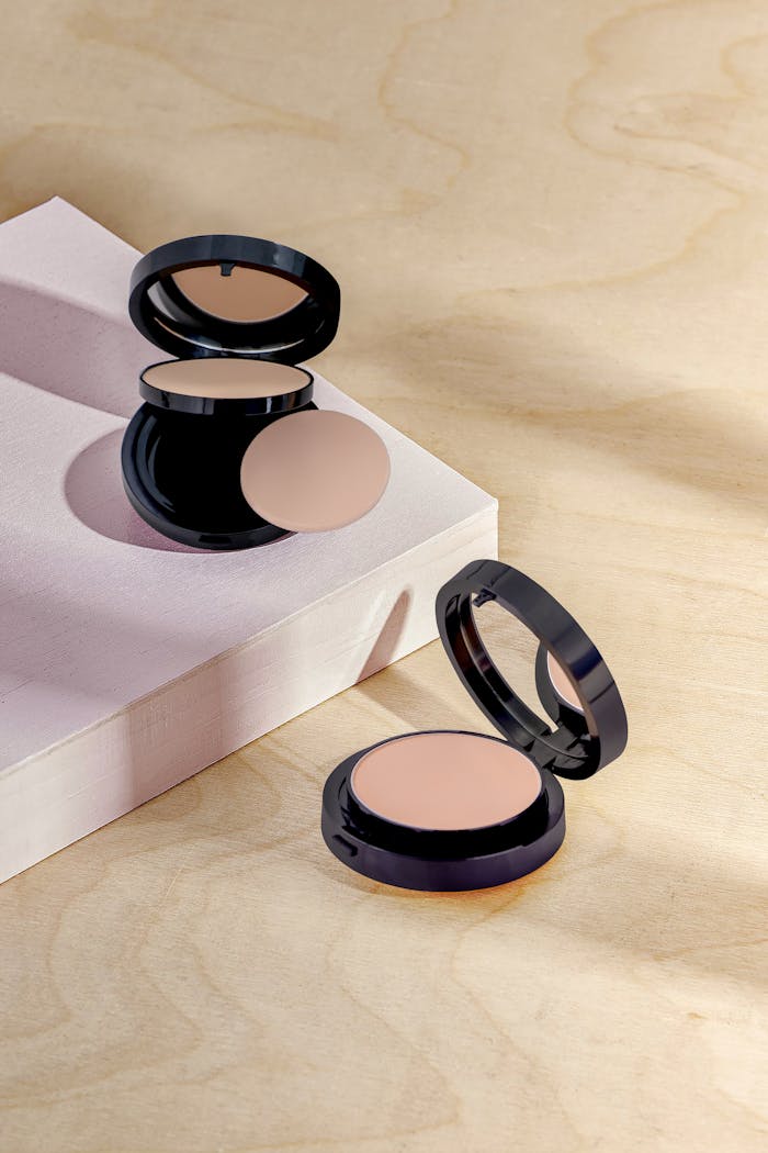 our-services-1 Open makeup compacts on a textured surface with soft lighting.