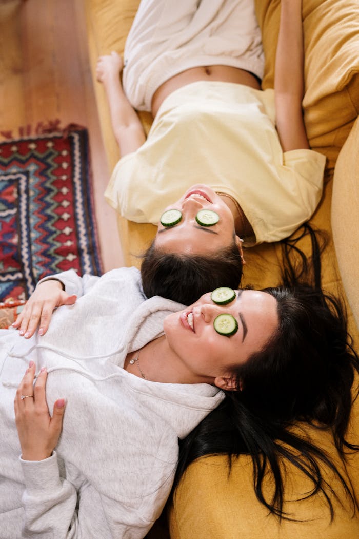gallery-1 Two women relaxing with cucumber eye masks on a sofa at home.