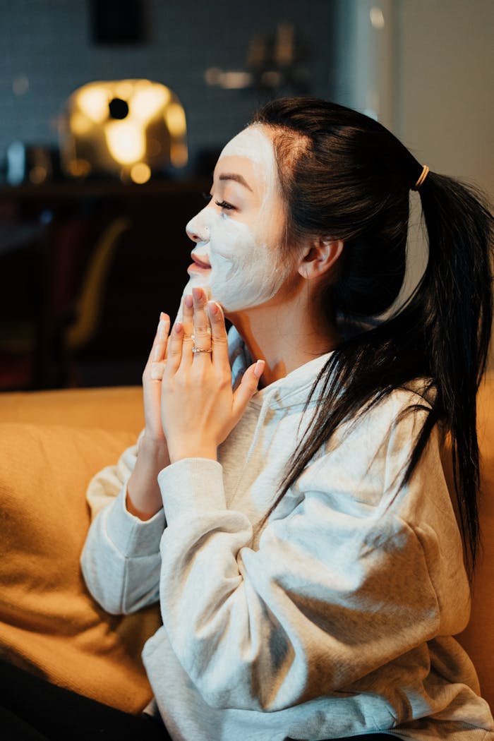 our-services-2 Asian woman relaxing with a face mask, practicing skincare in a cozy home environment.